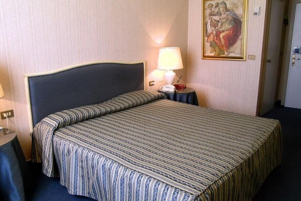 Elegantná hotelová izba s dvojlôžkom, lampou a obrazom na stene.  