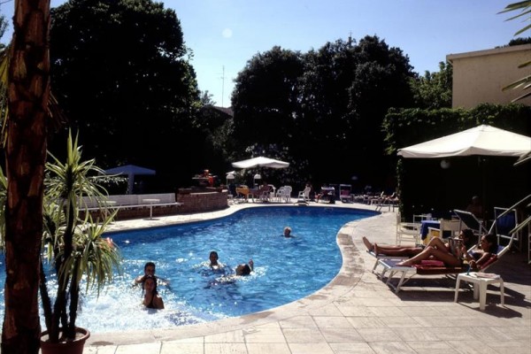 Ľudia relaxujú pri vonkajšom bazéne obklopenom stromami a slnečníkmi.