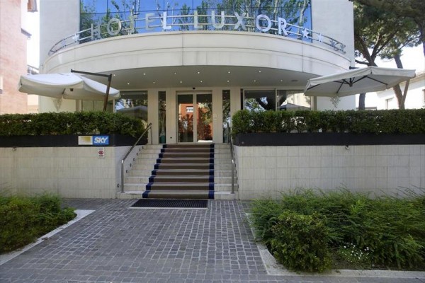 Vchod do moderného hotela s terasou a slnečníkmi.