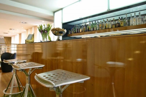 Moderný bar s dreveným pultom, kvetmi a fľašami alkoholu.