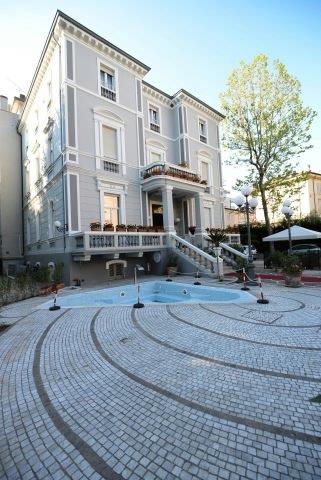 Sivobiela vila s fontánou a schodiskom v popredí.