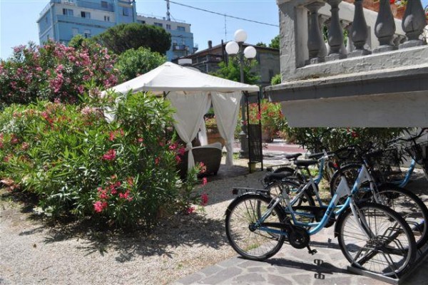 Stany a bicykle obklopené kvitnúcimi kríkmi v záhrade vedľa budovy.