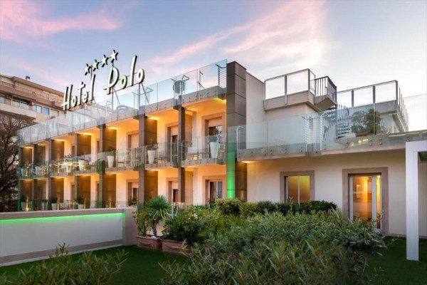 Moderná budova hotela s presklenými balkónmi a veľkým nápisom Hotel Polo na streche.