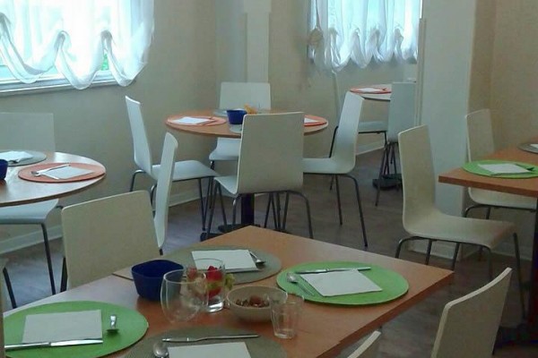 Jednoducho zariadená jedáleň s okrúhlymi stolmi a bielymi stoličkami.