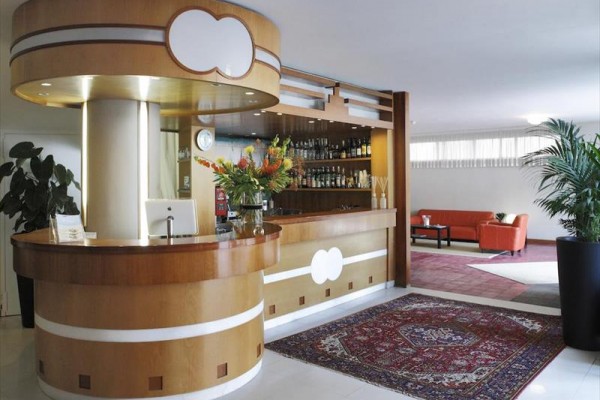 Lobby s okrúhlym recepčným pultom, kvetmi a červeným kobercom.