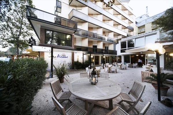 Moderný hotel s vonkajšou terasou a kruhovými drevenými stolmi.