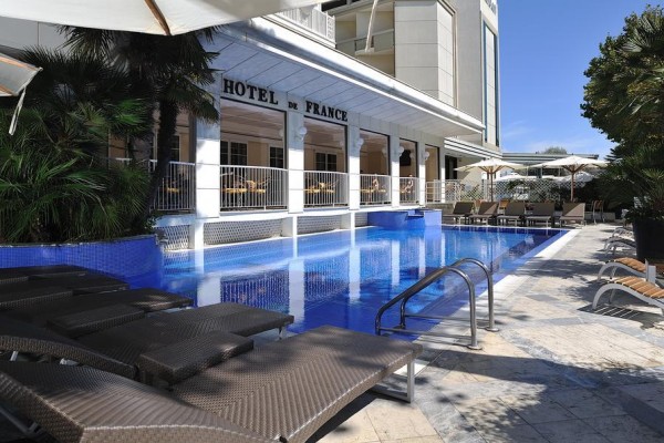 Vonkajší bazén s ležadlami pred hotelom s nápisom 