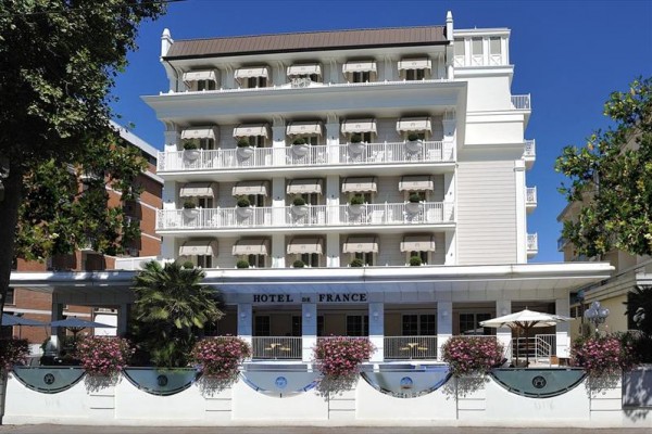 Bielo-modrý hotel s balkónmi, kvetmi a nápisom 