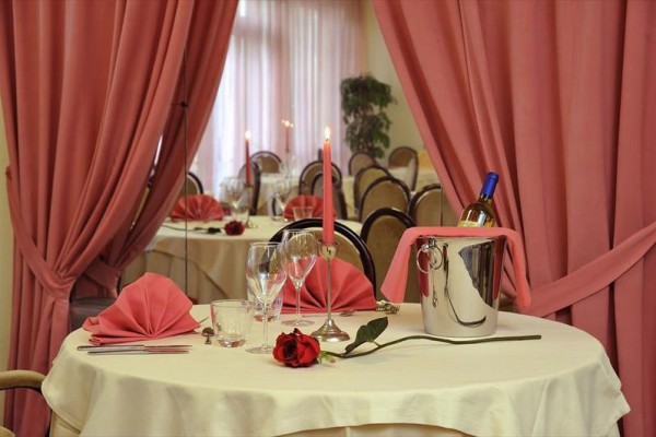 Elegantne prestretý stôl s ružou, sviečkou a šampanským v vedre, obklopený ružovými závesmi.
