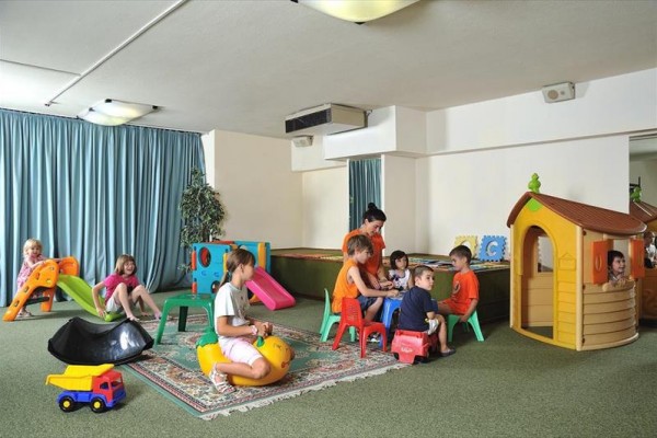 Deti sa hrajú v herni s rôznymi hračkami a atraktivitami vrátane hojdačky a šmykľavky.