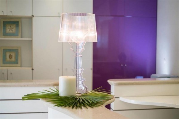 Stolná lampa s bielou sviečkou a zelenými listami na modernej recepcii s fialovou stenou.
