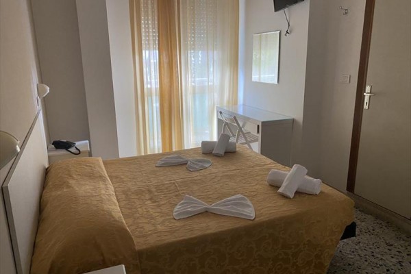 Spálňa s manželskou posteľou, zlatou prikrývkou a televíziou na stene.
