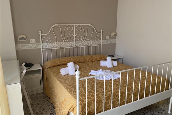 Kovová posteľ s béžovým obliekaním a poskladanými uterákmi na nej v spálni.
