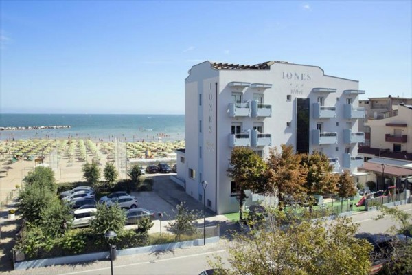 Hotel pri mori s plážou a zaparkovanými autami v popredí.