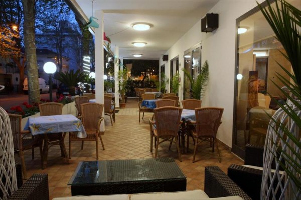 Nočná terasa s prútenými stoličkami a stolmi pozdĺž steny s kvetmi.