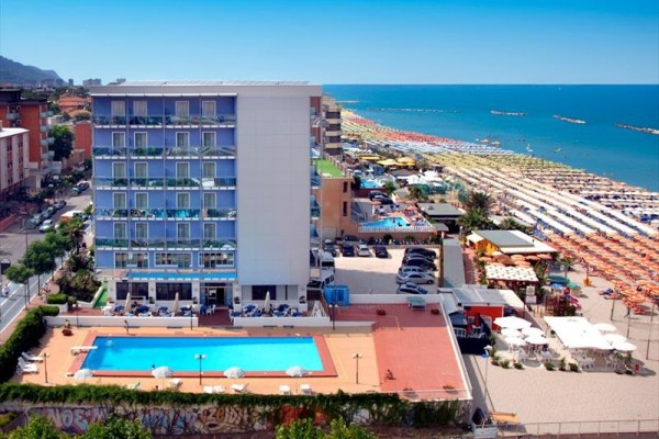 Moderný hotel s bazénom pri pláži s lehátkami a slnečníkmi.