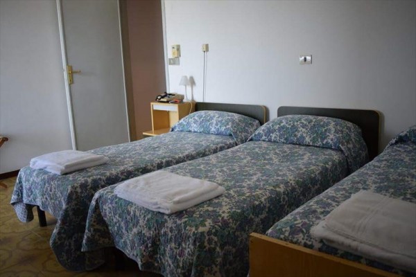 Tri jednolôžkové postele s kvetinovým prehozom a uterákmi v rade.
