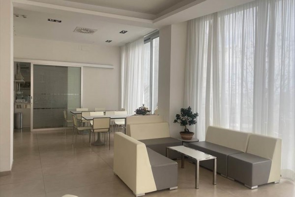 Moderný svetlý salónik s pohovkami a stolíkmi pri veľkých oknách.