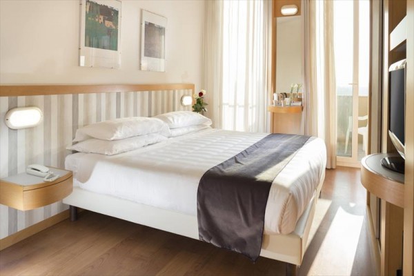 Hotelová izba s manželskou posteľou, nočnými stolíkmi a balkónom.