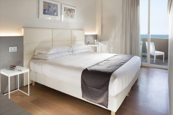 Moderná hotelová izba s manželskou posteľou a výhľadom na more z balkóna.