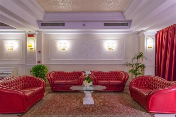 Červené kožené sedacie súpravy a sklenený stolík v elegantnej miestnosti s kobercami a rastlinami.