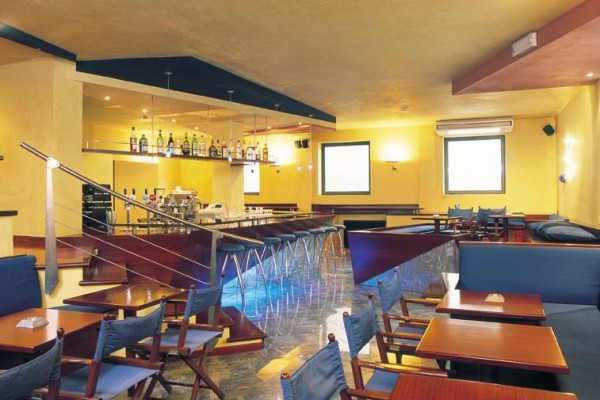 Moderný bar s vysokými stoličkami, drevenými stolmi a pohármi na pulte.