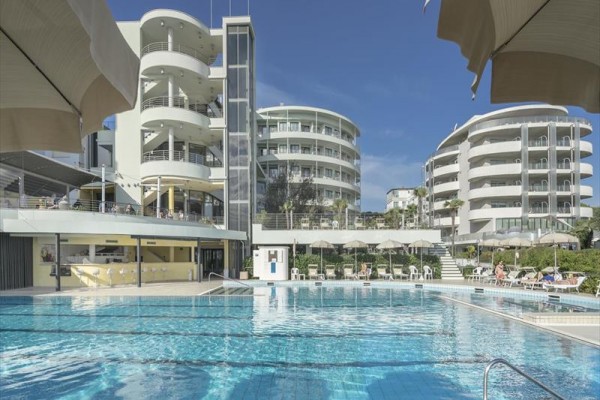 Moderné apartmány s bazénom obklopeným slnečníkmi.