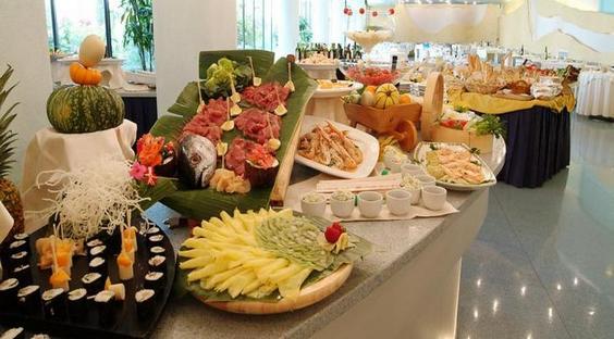 Bufetový stôl s rôznymi jedlami vrátane sushi, ovocia a mäsa.