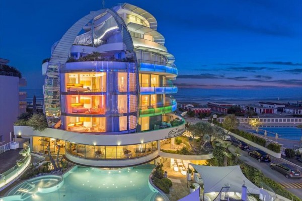 Moderný hotel s farebným večerným osvetlením a bazénom v popredí.