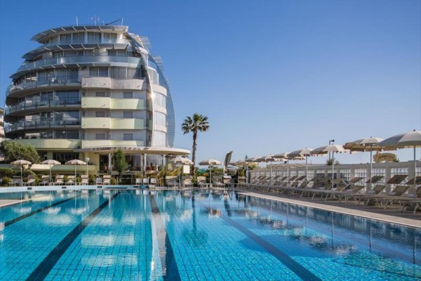 Moderný hotel s bazénom a ležadlami pod slnečníkmi.