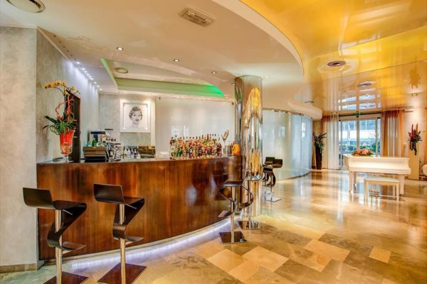 Štýlový moderný bar s dreveným pultom, vysokými stoličkami a bielym klavírom v pozadí.