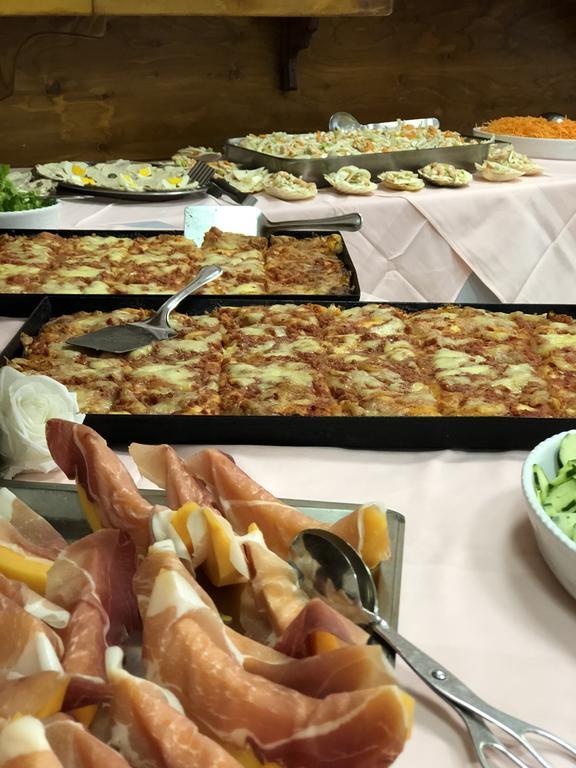 Stôl plný jedla vrátane misiek s oblohou so šunkou a pizzou.