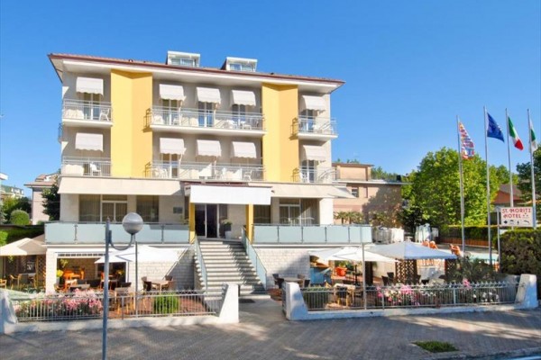 Štvorposchodový hotel so žltými balkónmi a slnečníkmi pred vchodom.