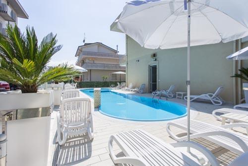 Ležadlá a slnečníky pri vonkajšom bazéne vedľa budovy.