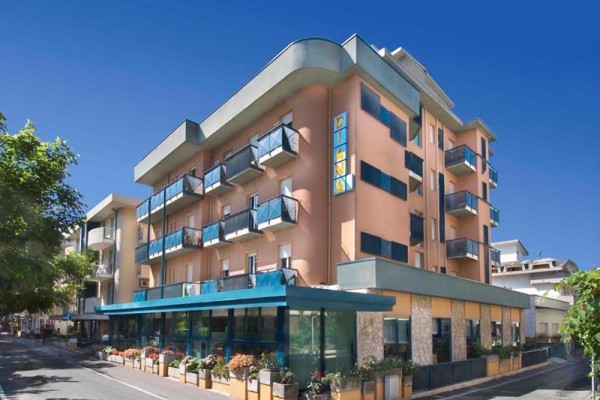 Moderný hotel s balkónmi a preskleným prízemím na rohu ulice za jasného počasia.