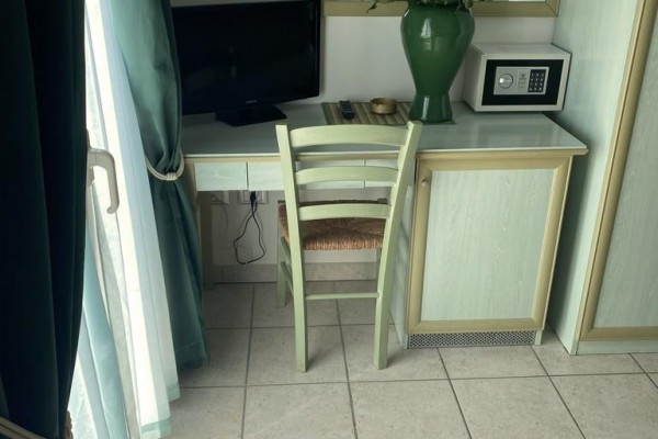 Stôl so stoličkou, počítačovým monitorom a vázou s kvetmi pri okne.