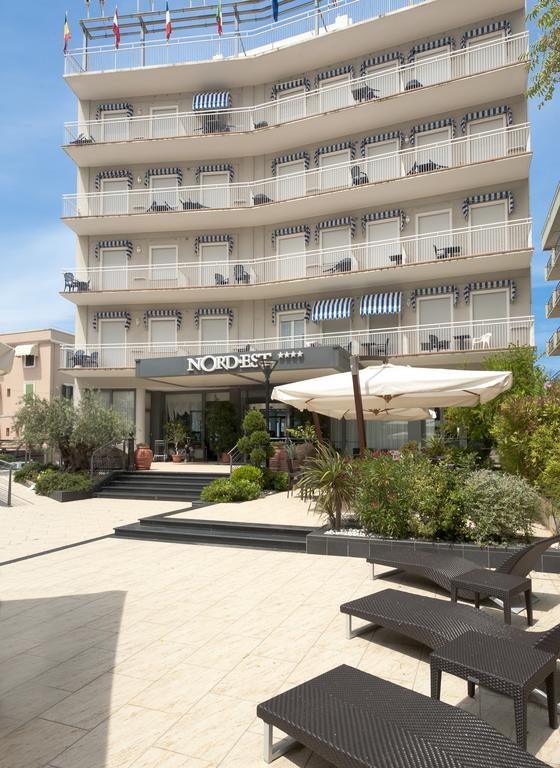 Budova hotela Nord Est s viacerými balkónmi a vonkajším posedením pod slnečníkom.