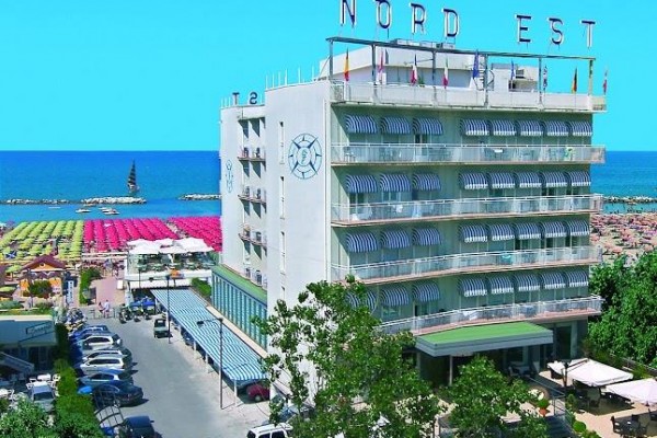 Hotel Nord Est pri pláži s farebnými slnečníkmi a modrou oblohou v pozadí.