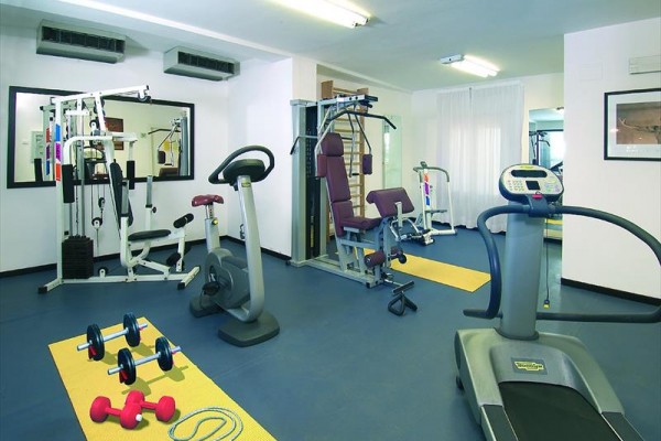 Posilňovňa s rôznorodým fitness vybavením, vrátane bežeckého pásu a činiek.