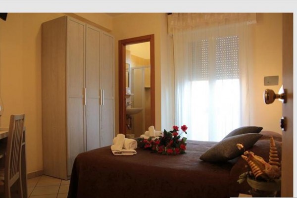 Izba s posteľou, kvetmi, skriňou a pohľadom do kúpeľne.