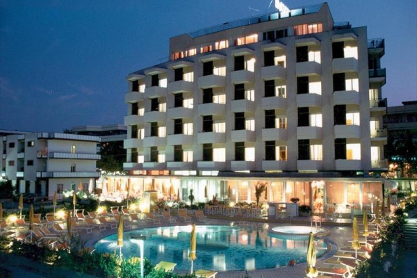 Hotel s osvetlenými oknami a vonkajším bazénom vo večerných hodinách.