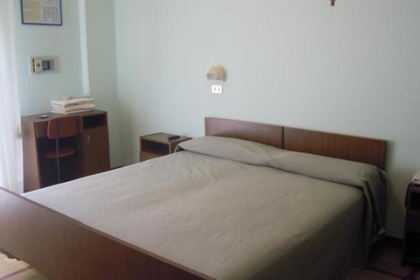 Hotelová izba s manželskou posteľou, stolom a stoličkou.