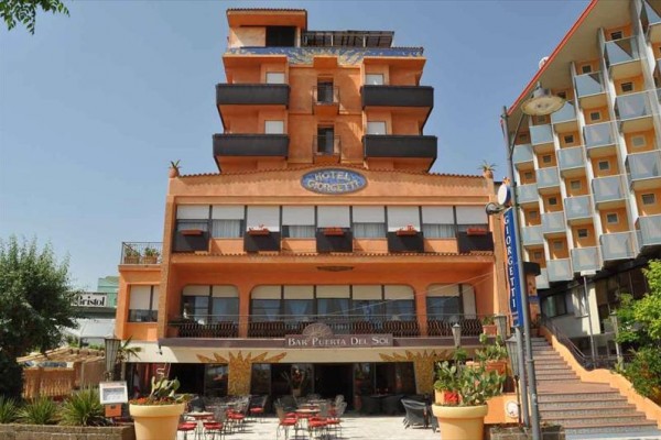 Päťposchodový oranžový hotel s barom na prízemí a vonkajším posedením.