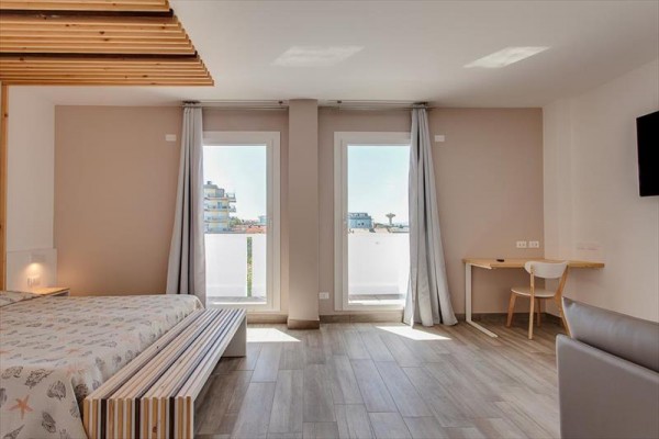 Moderná hotelová izba s veľkými oknami a výhľadom na mesto.  
