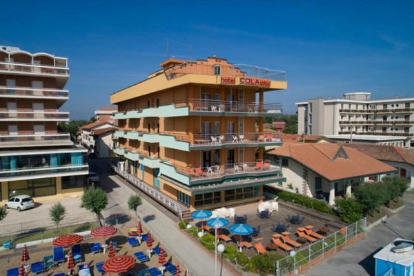 Hotel Cola s balkónmi a terasou, obklopený lehátkami a slnečníkmi.