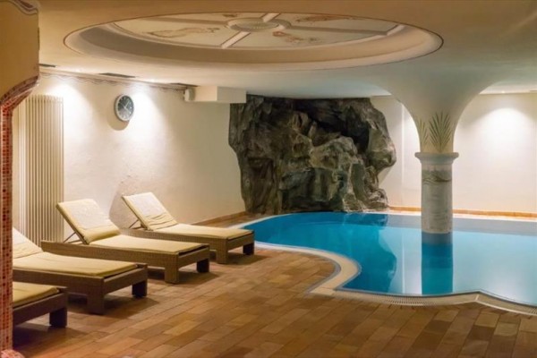 Krytý bazén s ležadlami a umelou skalnou dekoráciou.