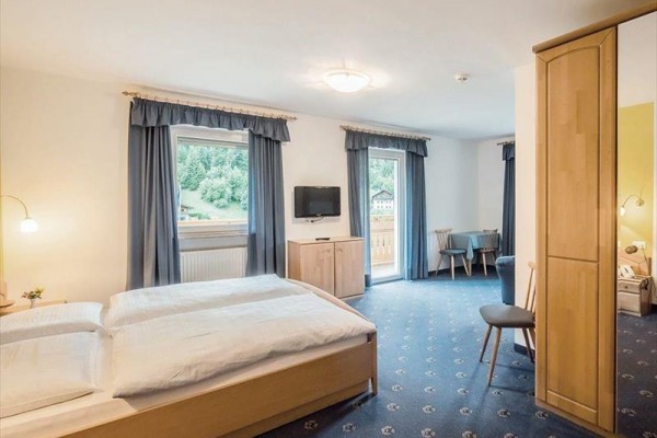 Svetlá izba s dvojlôžkom, televíziou a balkónom, s výhľadom na zelenú krajinu.