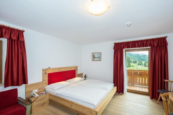 Izba s drevenou posteľou, červenými závesmi a balkónom s výhľadom na krajinu.