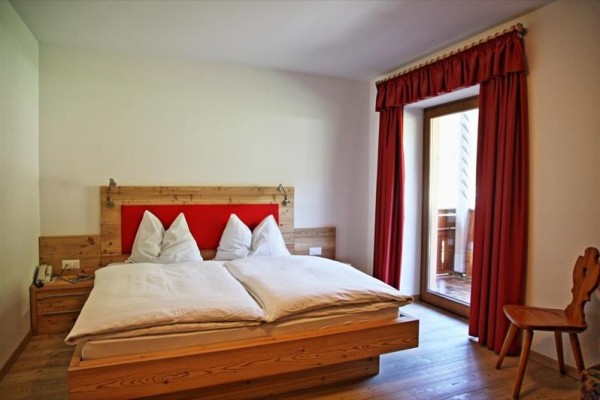 Dvojlôžková posteľ v hotelovej izbe s červenými závesmi pri balkóne.