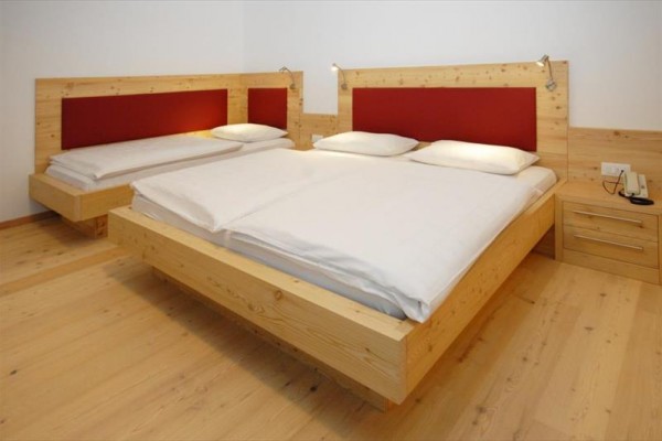 Izba s dvoma drevenými posteľami s bielou posteľnou bielizňou a červenými čelami.